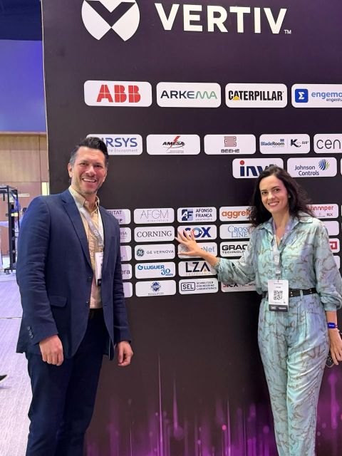 Gustavo Gasparoto e Fabíola Andretto diante do painel de patrocinadores do DCD Connect LATAM 2026, com a marca AFGM entre as empresas listadas